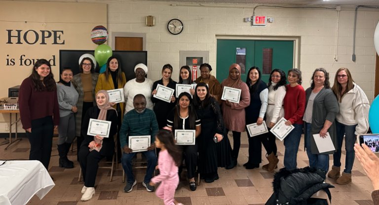 A group of people pose indoors, some seated and some standing, holding certificates. A child walks in front. The background has a sign reading "HOPE is found". A group of people pose indoors, some seated and some standing, holding certificates. A child walks in front. The background has a sign reading "HOPE is found".